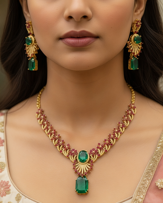 Woman wearing a gold necklace with emerald green stones and matching earrings.