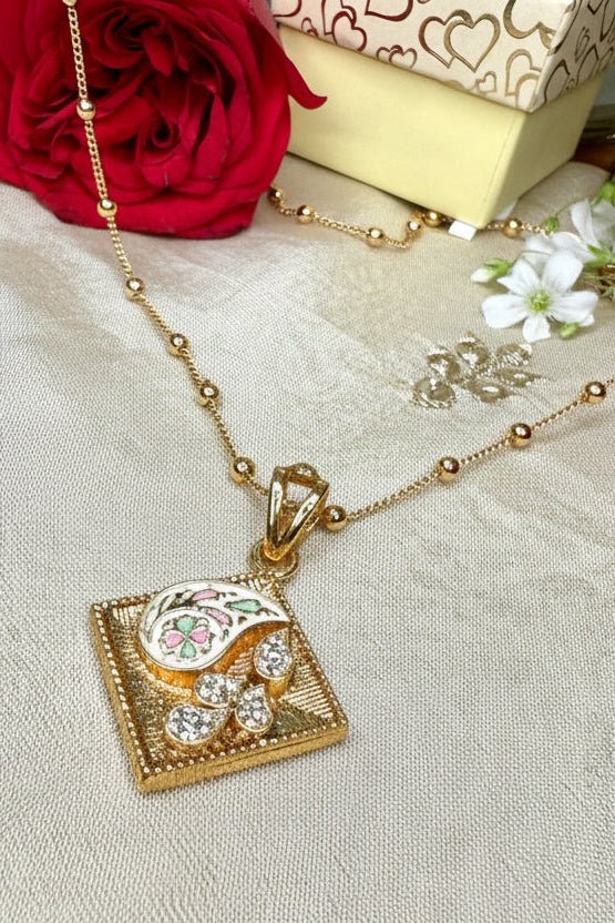 Gold pendant set with a decorative pendant on a textured surface with flowers and jewelry.