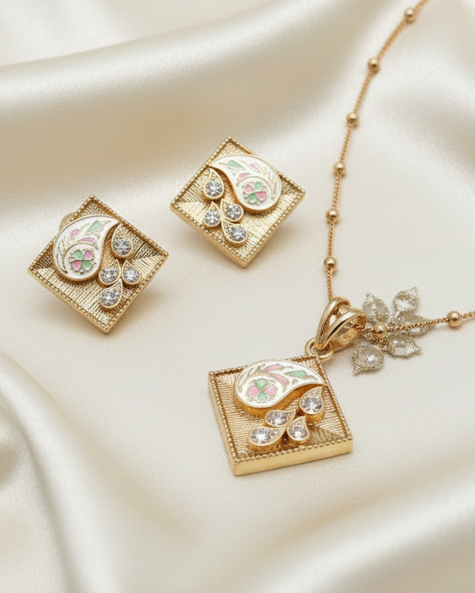 Gold necklace with square pendant with earringson a textured surface with a decorative box in the background.