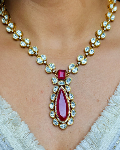 Gold necklace with a red gemstone pendant on a person wearing a white lace garment.