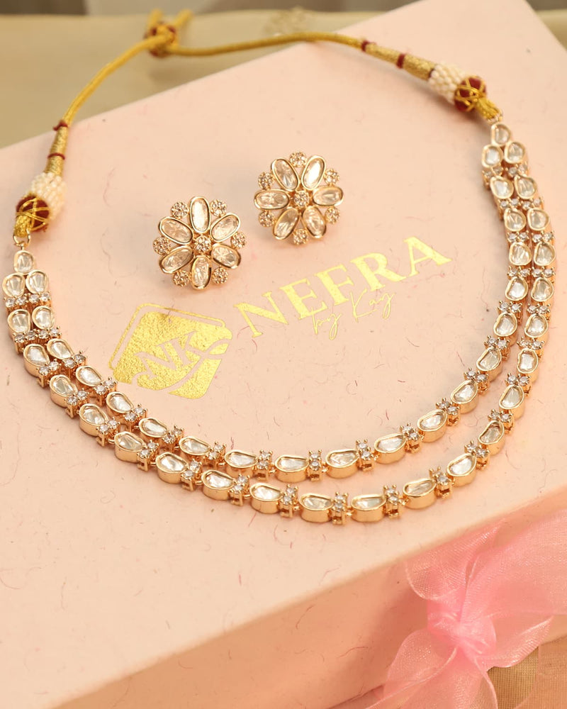 Gold necklace and earrings set on a pink box with 'NEFRA' branding.