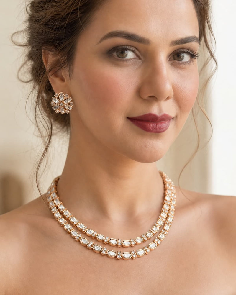 A close-up of a woman wearing a double-strand rose gold and crystal necklace with matching crystal flower-shaped stud earrings.